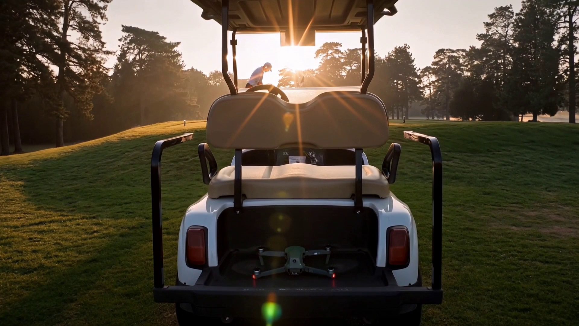 A golf cart at dawn with the Caddi drone in its bed and a golfer on the tee beyond.